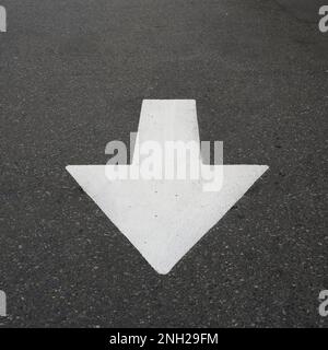 Der weiße Verkehrspfeil auf dem grauen Asphalt weist die Fahrzeuge an, geradeaus zu fahren. Stockfoto