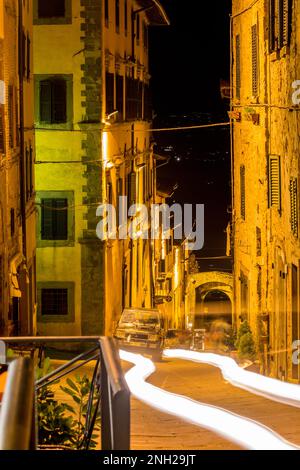 Toskana, Italien. Nachtfoto mit langen Belichtungszeiten und Autostrecken, Blick auf die Altstadt mit Sternenlicht. Warme Töne und Stimmung. Straßenfoto. Stockfoto