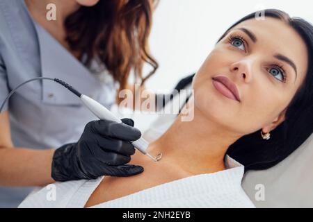 Schöne weiße junge Frau führt eine Leberfleckenentfernung in einer modernen Kosmetik-Hautklinik durch. Behandlung von Hautflecken mit Laser Met Stockfoto