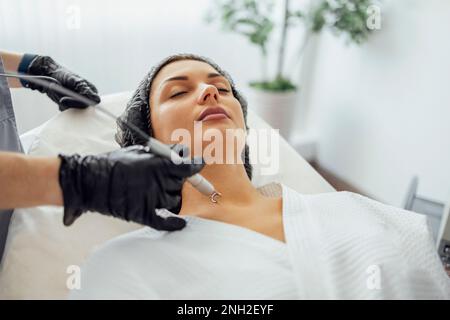 Schöne weiße junge Frau führt eine Leberfleckenentfernung in einer modernen Kosmetik-Hautklinik durch. Behandlung von Hautflecken mit Laser Met Stockfoto