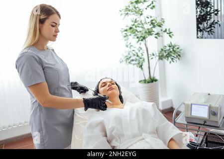 Schöne weiße junge Frau führt eine Leberfleckenentfernung in einer modernen Kosmetik-Hautklinik durch. Behandlung von Hautflecken mit Laser Met Stockfoto