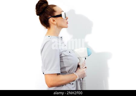 Junge Frau Kosmetikerin in medizinischen Uniform Einstellmaschine für Fotorejuvenation oder Laser-Haarentfernung während der Wartezeit auf den nächsten Kunden in Spa-Salon, Stockfoto