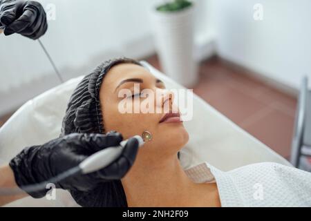 Schöne weiße junge Frau führt eine Leberfleckenentfernung in einer modernen Kosmetik-Hautklinik durch. Behandlung von Hautflecken mit Laser Met Stockfoto