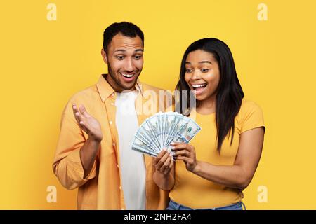 Glückliche, schockierte junge afroamerikanische Männer und Frauen, die viel Geld in der Hand haben, freuen sich über den Sieg Stockfoto
