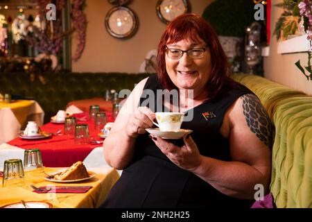 Eine Frau, die sich in einem farbenfrohen und gemütlichen Café entspannt und Tee aus einer Tasse trinkt. Manchester. Vereinigtes Königreich. Stockfoto