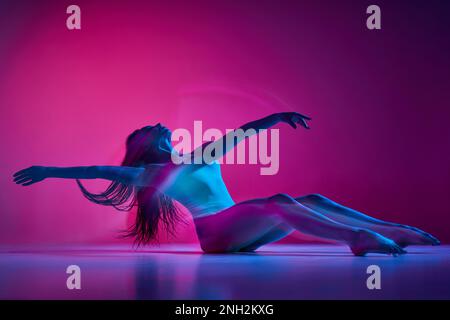 Selbstliebe. Freistil. Junge Frau tanzt im Body über einem abgestuften pinkfarbenen Studiohintergrund in Neon mit gemischten Lichtern. Konzept der Tanzästhetik, Kunst Stockfoto