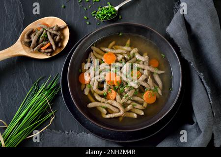 Bayerisches, schwäbisches und österreichisches Gericht: Leberspaetzle in einer Rindersuppe auf einem dunklen Schieferteller Stockfoto