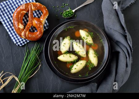 Bayerisches, schwäbisches und österreichisches Gericht - Grießklöße in Gemüsebrühe, serviert mit knuspriger Brezel Stockfoto