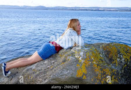 An einem wunderschönen Oktobertag in Wormit Beach, Fife, liegt Rhianna Martin auf großen Felsen neben dem Fluss Tay, Schottland Stockfoto