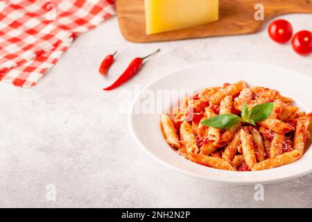 Klassische italienische Pasta Penne alla arrabiata mit frischem Basilikum auf hellem Hintergrund, selektiver Fokus Stockfoto