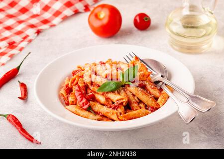 Klassische italienische Pasta Penne alla arrabiata mit frischem Basilikum auf hellem Hintergrund, selektiver Fokus Stockfoto