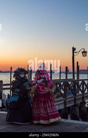 Karnevalsbesucher, gekleidet in prächtigen Kostümen und Masken während des Karnevals 2023 in Venedig, Sonnenaufgang am Markusplatz, Venedig, Italien im Februar Stockfoto