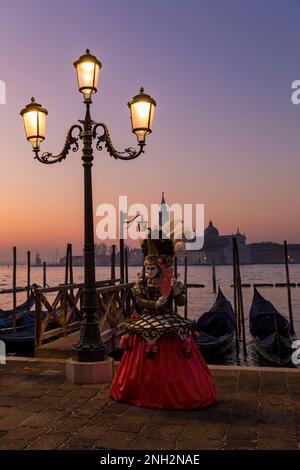 Karnevalsbesucher gekleidet in prächtigen Kostümen und Maske während des Karnevals 2023 am frühen Sonnenaufgang am Markusplatz, Venedig, Italien im Februar Stockfoto