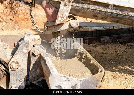 Betonmischwagen zum Gießen von frischem nassem Beton in Baggereimer auf einer Baustelle Stockfoto