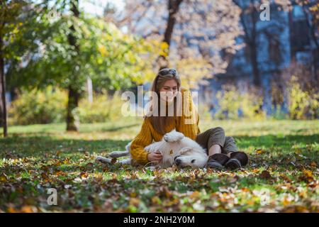 Belgrad, Serbien. 10. November 2022. Fröhliche junge Frau streichelte ihren Hund, während sie an einem sonnigen Tag auf dem Boden in einem Park saß. Stockfoto