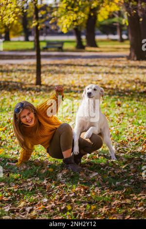 Belgrad, Serbien. 10. November 2022. Wunderschöne junge Frau, die mit ihrem goldenen Retriever auf dem Boden eines Parks spielt und lächelt. Spaß am sonnigen Tag. Stockfoto