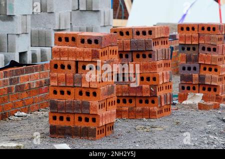 Rote Steine und Betonblöcke, die auf der Baustelle geliefert und neben dem Arbeitsort für Maurer aufgestellt wurden Stockfoto