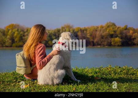 Belgrad, Serbien. 10. November 2022. Wunderschöne junge Frau, die ihren süßen goldenen Retriever umarmt und an einem sonnigen Tag den Sava Revier schaut. Stockfoto