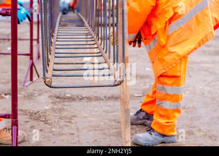 Bauarbeiter, die Stahlverstärkerstäbe auf der Baustelle befestigen. Stahlfixiervorrichtung zur Montage des Verstärkungskäfigs von Armierungsstäben. Selektiver Fokus Stockfoto