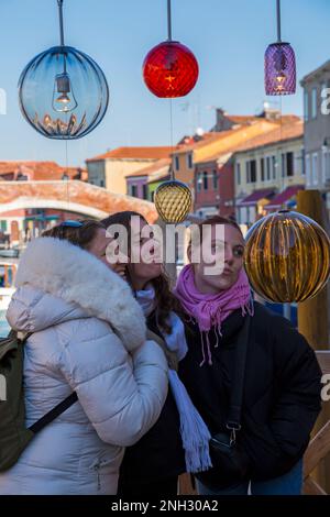 Drei junge Touristen posieren im Februar in Murano, Venedig, Italien, mit Murano-Glaslichtern und Reflexionen Stockfoto