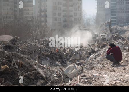 Kharamanmaras, Türkei. 18. Februar 2023. Ein Mann sitzt neben seinem eingestürzten Haus, während ein Suchteam nach Menschen unter den Trümmern im Epizentrum des Erdbebens sucht. Kredit: Ahmed Deeb/dpa/Alamy Live News Stockfoto