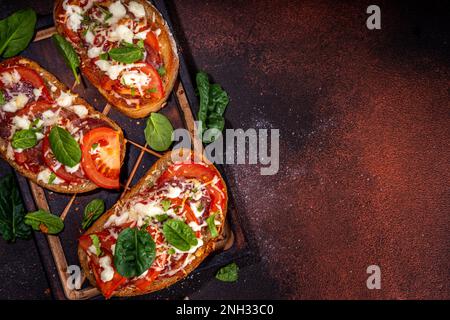 Warme Pizza-Sandwiches mit Tomaten, Mozzarella-Käse und Peperoni auf dunklem Hintergrund mit Kräutern, Olivenöl und Gewürzen Stockfoto