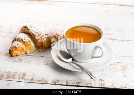 Frühstück mit einer Tasse Tee und Croissant auf einem Holztisch. Stockfoto
