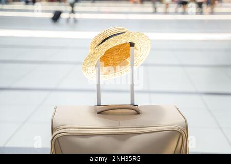 Strohhut auf einem großen Koffer, Tasche im Flughafenterminal. Warten auf Boarding zum Flug. Familienurlaub. Gepäckaufgabe in der Abflughalle. S Stockfoto