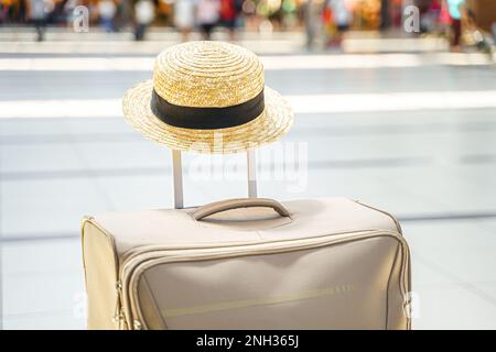 Strohhut auf einem großen Koffer, Tasche im Flughafenterminal. Warten auf Boarding zum Flug. Familienurlaub. Gepäckaufgabe in der Abflughalle. S Stockfoto