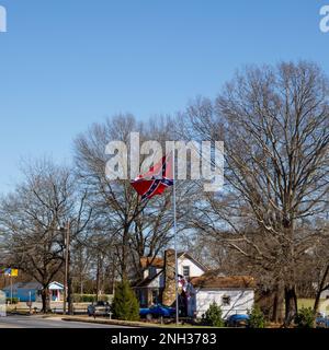 HICKORY, NC, USA-18. FEBRUAR 2023: Älteres Felsenhaus mit großer Konföderiertenflagge an der hohen Fahnenstange. Sonniger, blauer Himmel. Quadratisches Bild. Stockfoto