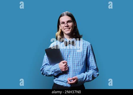 Ein schlauer Student mit Laptop, der in die Kamera schaut, blauer Hintergrund Stockfoto