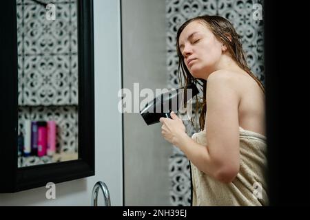 Frau in Handtuch eingehüllt, die Haare im Bad trocknet. Weibliche Morgenhygiene und Haarpflege Stockfoto