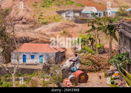 Eine Frau arbeitet vor einem einfachen Haus im rauen und bergigen Zentrum von Santiago Island, Kap Verde Inseln, Makaronesien Stockfoto