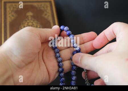 Die Hand der muslime betet mit Rosenkranz auf koranischem Hintergrund. islamischer Konsept Stockfoto