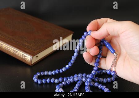 Die Hand der muslime betet mit Rosenkranz auf koranischem Hintergrund. islamischer Konsept Stockfoto