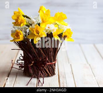 Narzissen in einer Zweigvase auf dem Holztisch Stockfoto