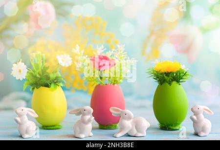Osterdekoration mit Frühlingsblumen in bunten gefärbten Eiern und weißen osterkaninchen Stockfoto