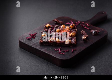 Handgemachte Schokolade mit Beeren, Nüssen und Gewürzen auf dunklem Betonhintergrund. Süßigkeiten, die zu Hause hergestellt werden Stockfoto