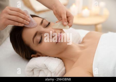 Junge Frau, die im Schönheitssalon eine Gesichtsmassage mit Gua-sha-Werkzeugen erhält Stockfoto
