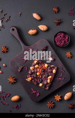 Handgemachte Schokolade mit Beeren, Nüssen und Gewürzen auf dunklem Betonhintergrund. Süßigkeiten, die zu Hause hergestellt werden Stockfoto