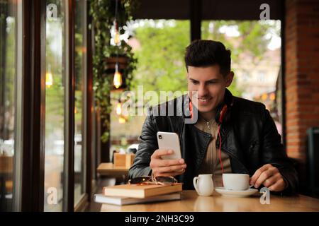 Mann mit Kopfhörern und Smartphone am Tisch im Café Stockfoto