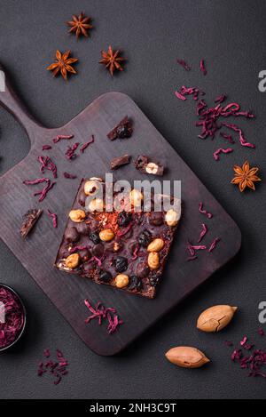 Handgemachte Schokolade mit Beeren, Nüssen und Gewürzen auf dunklem Betonhintergrund. Süßigkeiten, die zu Hause hergestellt werden Stockfoto