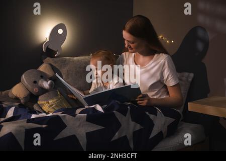 Mutter und Kind lesen Buch im Zimmer mit raketenförmiger Nachtlampe Stockfoto