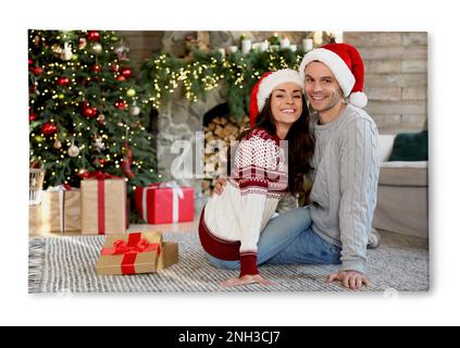 Foto auf Leinwand, weißer Hintergrund. Glückliches junges Paar mit Weihnachtsmannmützen im Wohnzimmer, dekoriert für Weihnachten Stockfoto