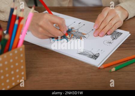 Junge Frau, die Anti-Stress-Seite am Tisch ausmalt, Nahaufnahme Stockfoto