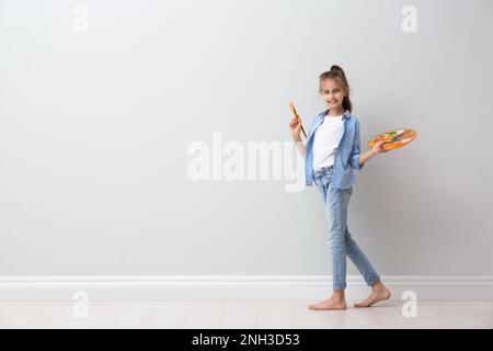 Kleines Mädchen mit Pinsel und Farbpalette in der Nähe von hellen Wänden in Innenräumen. Platz für Text Stockfoto