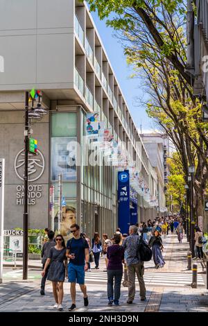 Tokio. Tagsüber Blick entlang Pflaster überfüllt mit Menschen zu Fuß und Äußere der Omotesando Hills Shopping Complex. Blauer Himmel, Frühling. Stockfoto