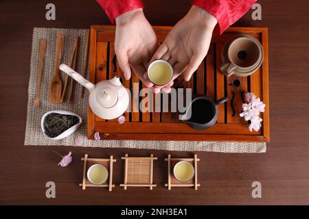 Frau mit einer Tasse frisch gebrühtem Getränk während der traditionellen Teezeremonie am Holztisch, Draufsicht Stockfoto