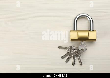 Modernes Vorhängeschloss mit Schlüsseln auf weißem Holztisch, Draufsicht. Platz für Text Stockfoto