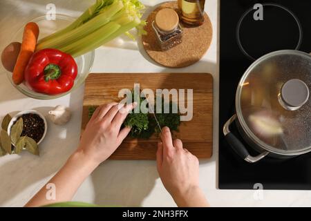 Eine Frau schneidet Dill, um Bouillon auf der Arbeitsfläche zu machen, Draufsicht. Hausgemachtes Rezept Stockfoto